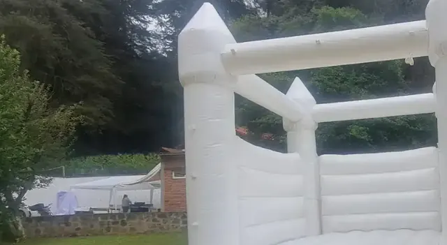 Castillo inflable blanco en un jardín rodeado de árboles