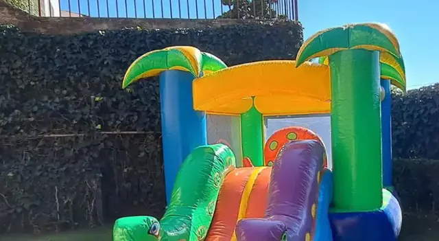Inflable con palmeras y resbaladilla instalado en un jardín