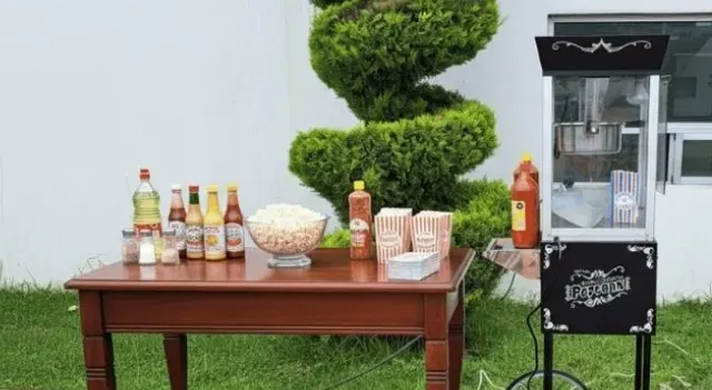 Mesa con palomitas, conos y salsas junto a la máquina de palomitas en un jardín