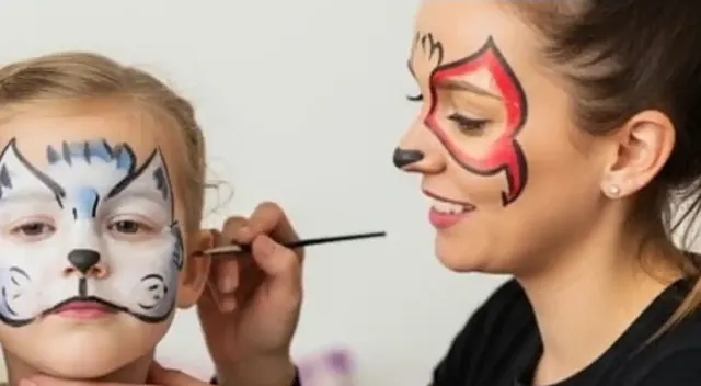 Niña con la cara pintada de gatito junto a la pintacaritas con un diseño de colores
